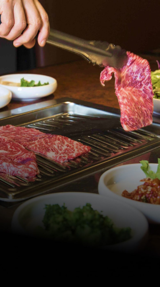 Hand grilling marbled Korean BBQ beef with side dishes at Geonbae Frankston VIC