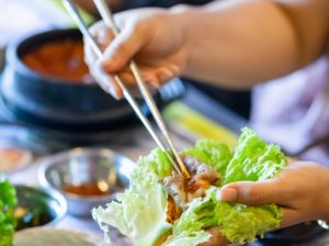 Hand preparing a Korean BBQ lettuce wrap with pork and kimchi at Geonbae Frankston VIC